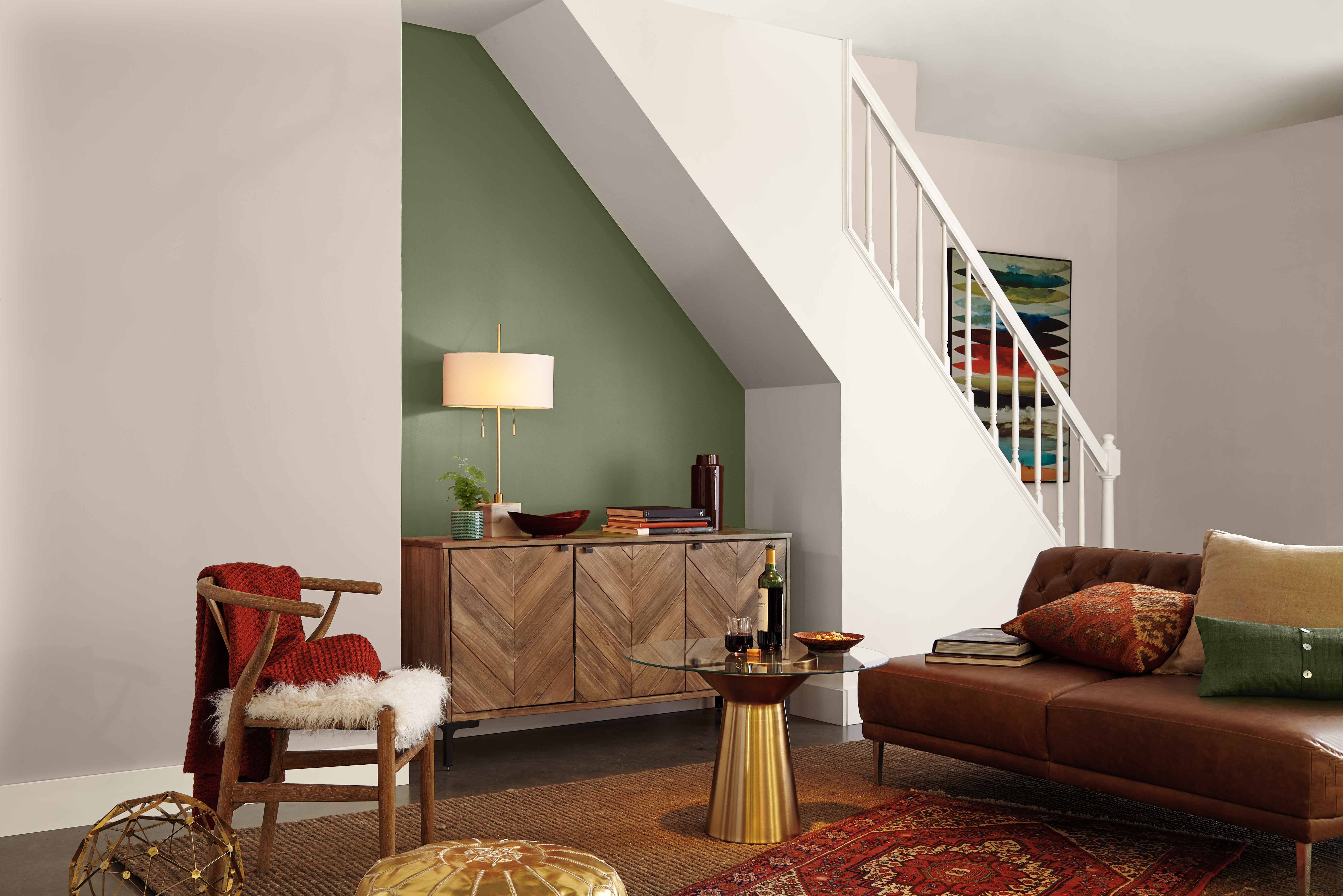 Cette image montre un espace de vie aménagé au sous-sol avec un canapé en cuir et une décoration à la fois chaleureuse et soignée. Sous l’escalier, on aperçoit un mur d’accent peint en un vert terreux appelé «Écologique», devant lequel se dresse un bahut en marqueterie.