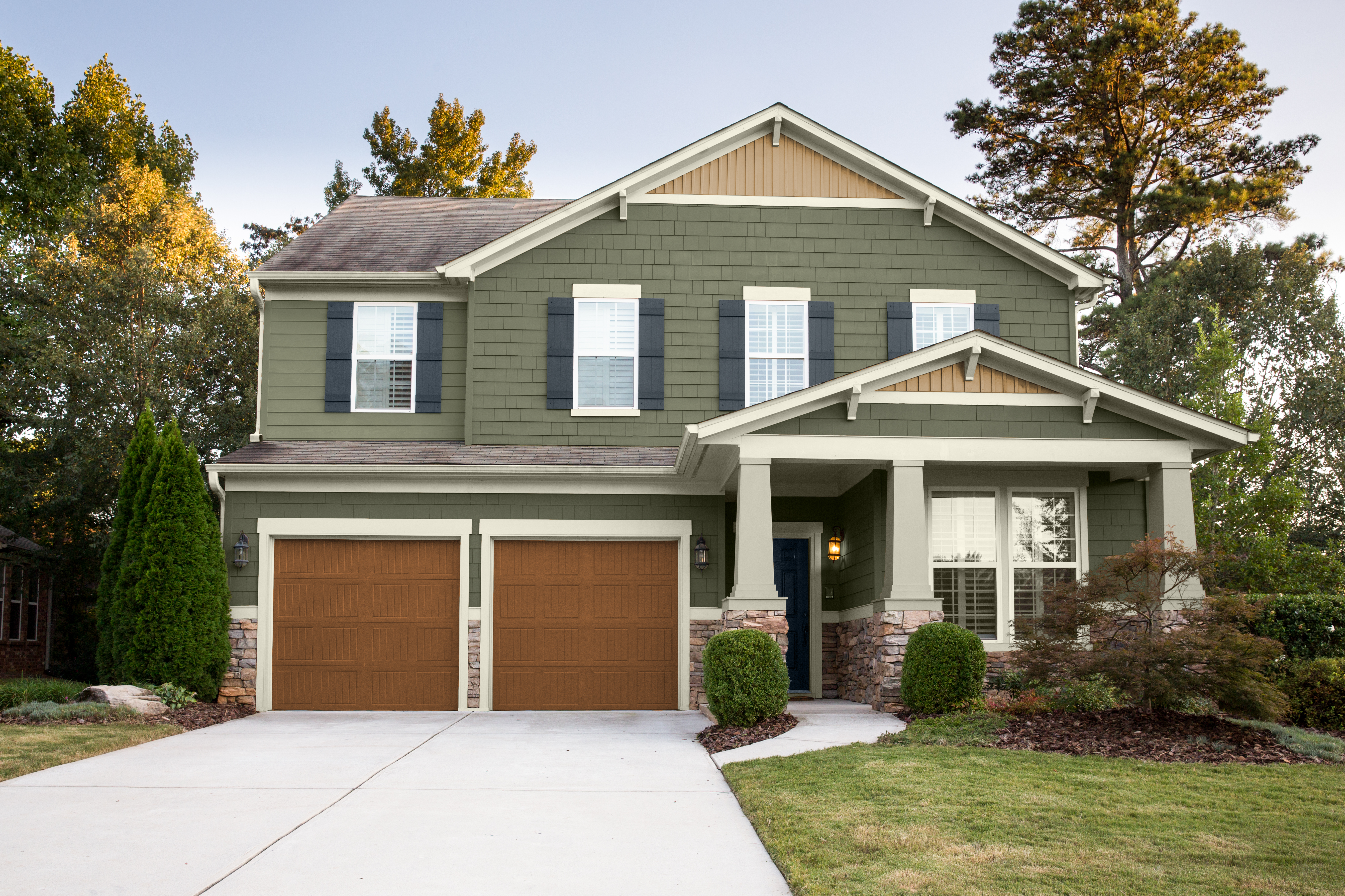 Cette image montre une maison de style Craftsman presque entièrement peinte en vert, avec un garage double, un grand porche couvert et un aménagement paysager en devanture.