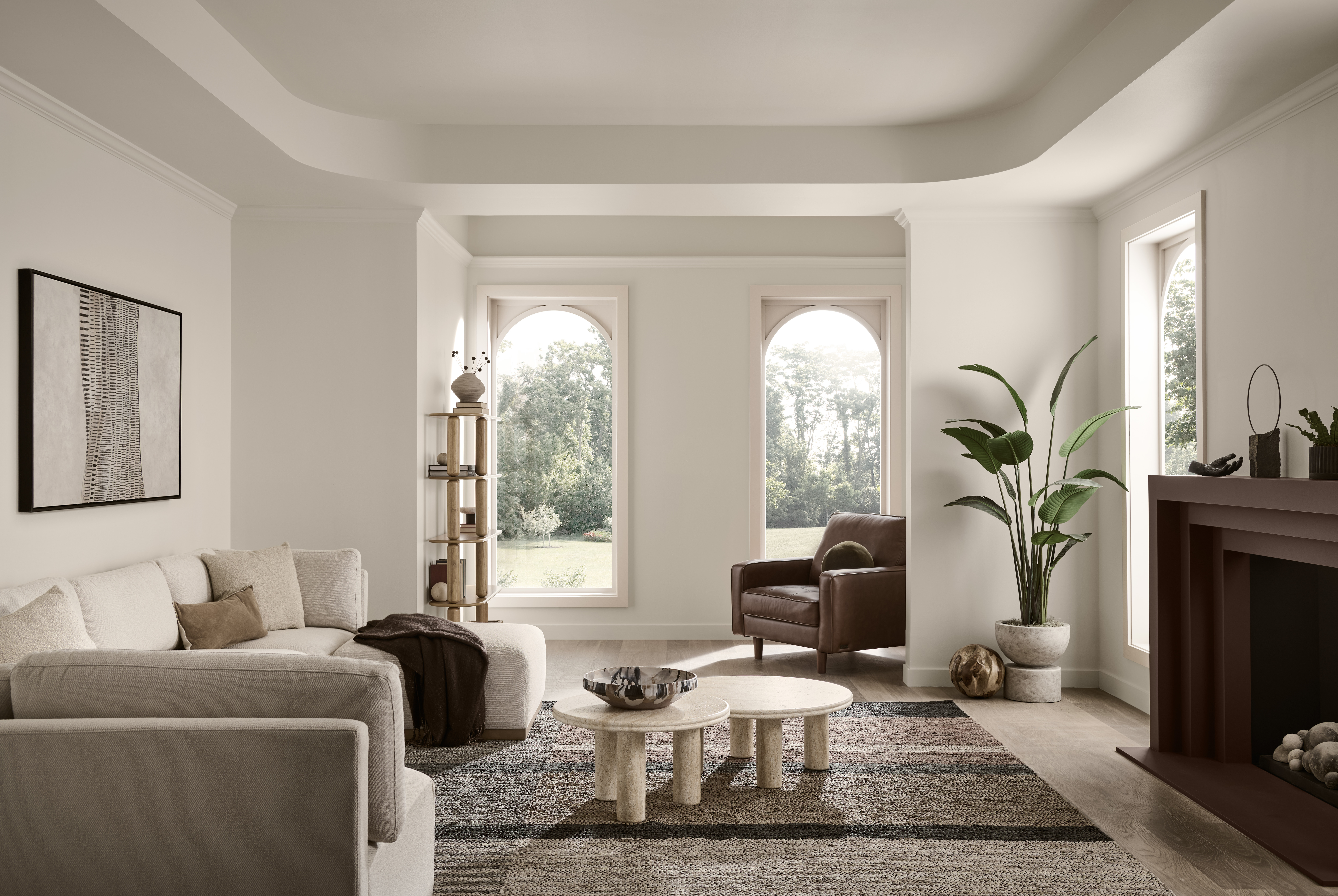 Cette image montre un salon où plusieurs teintes de peinture neutres sont mises en valeur. Les murs peints en Pain de blé sont ajourés de fenêtres cintrées, tandis qu’une table à café de style moderne se dresse entre un canapé de couleur pâle et une cheminée brun foncé, le tout rehaussé de chaleureux accents de bois et de textures superposées de couleur neutre.