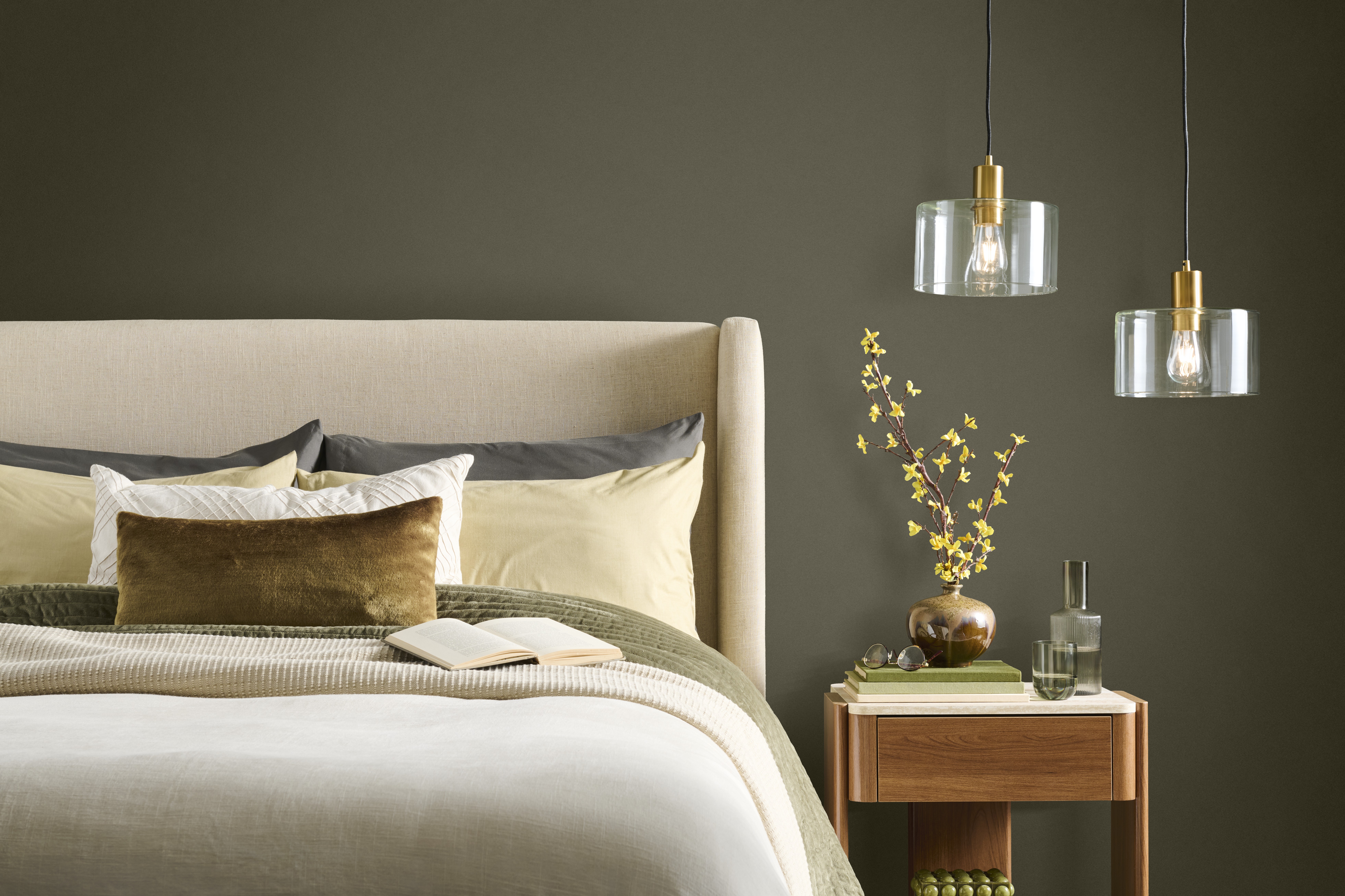 Cette image montre une chambre à coucher paisible au décor contemporain avec un mur d’accent peint en teinte Terre à terre de BEHR, un lit à tête rembourrée de couleur neutre, une épaisse literie, une table de chevet en bois et des luminaires suspendus en verre.