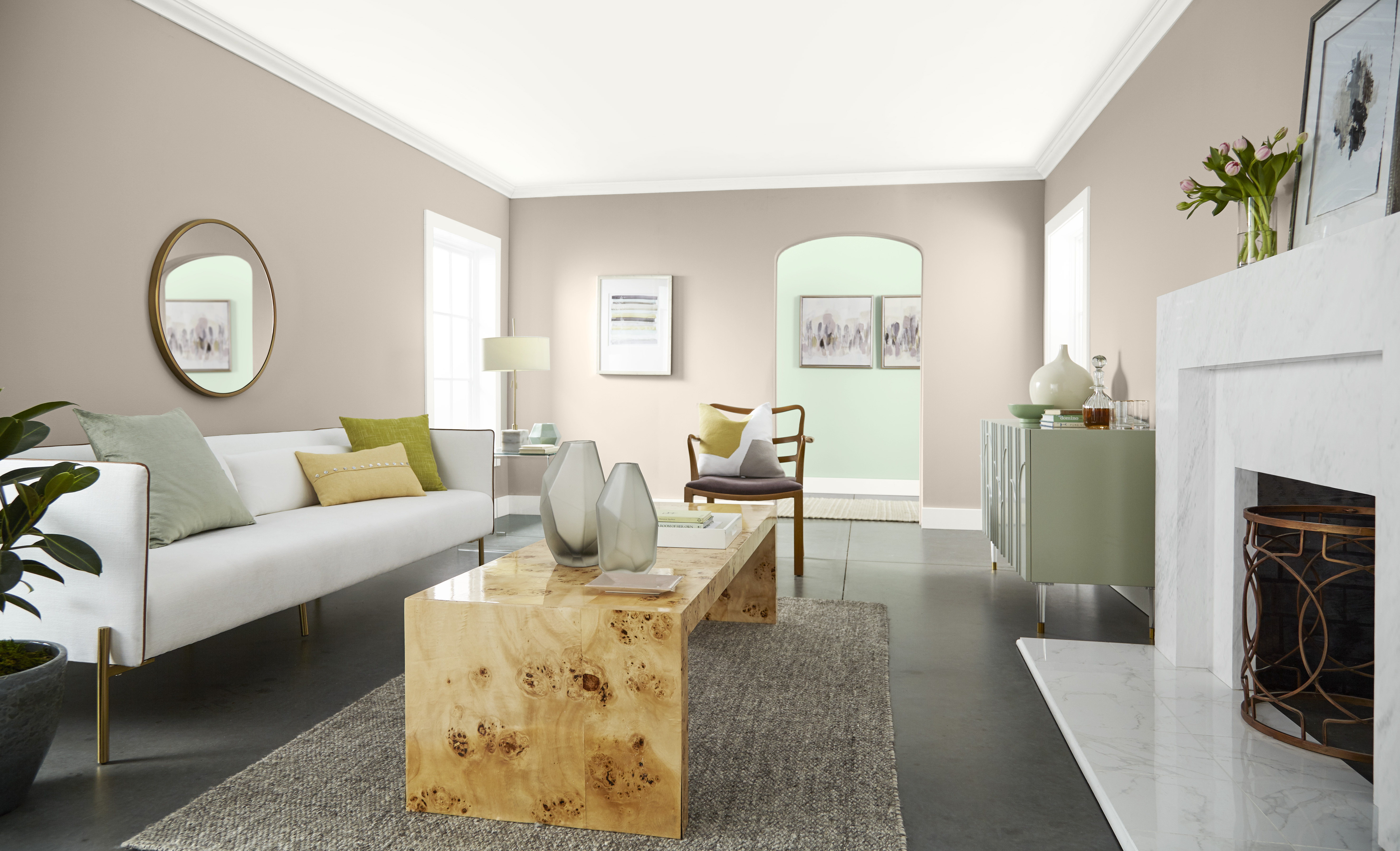 Cette image montre un salon avec des murs peints en teinte Pain de blé, un canapé blanc, une table basse en bois naturel, un tapis gris, une cheminée blanche et des accessoires décoratifs dans des tons de vert tendre.