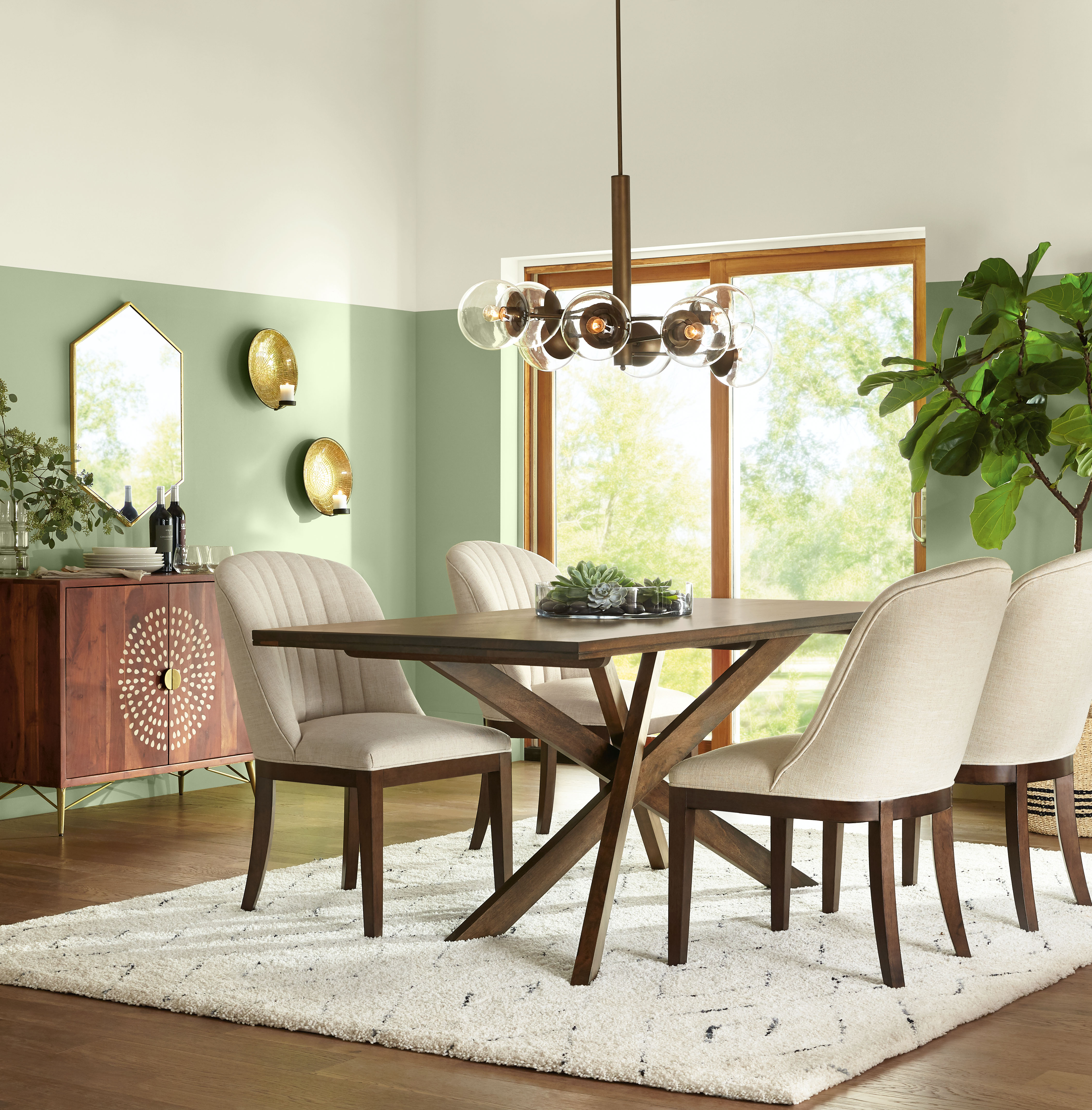 Cette image montre une salle à manger décorée de murs verts peints en Aneth haché et meublée d’une table en bois naturel et de chaises rembourrées de couleur crème. Les accents métalliques ajoutent une touche de chaleur à ce décor biophilique.
