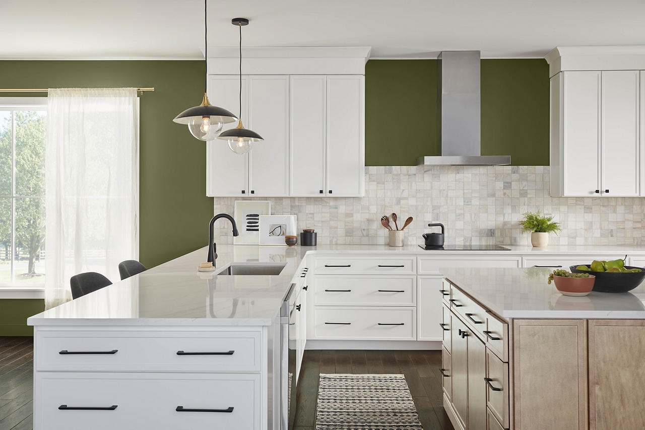 Cette image montre une cuisine spacieuse et aérée avec des murs vert olive, des armoires blanches aux poignées noires, un îlot en bois clair et des comptoirs en quartz blanc. Le vert olive apporte une chaleur naturelle et une sophistication terre à terre, créant une ambiance accueillante et ancrée dans la nature. Accompagnée d’armoires blanches comme neige et de tons de bois clair, cette teinte ajoute de la profondeur et du contraste à l’espace, ainsi qu’une touche de beauté organique et pérenne.