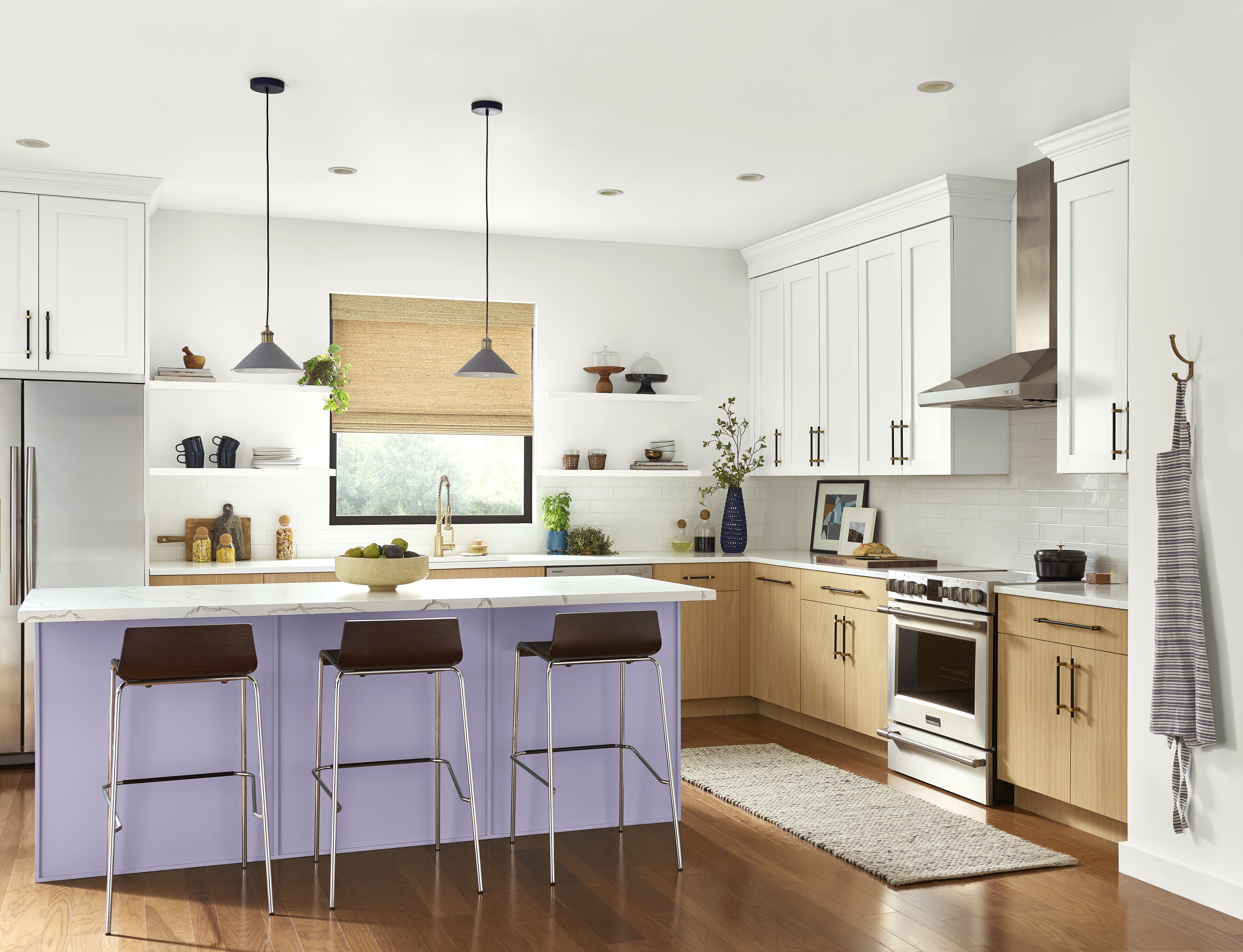 Cette image montre une cuisine avec un îlot de couleur lavande, des armoires du haut blanches, des armoires du bas en bois naturel, des comptoirs blancs, des luminaires suspendus et un parquet au ton chaud. La teinte lavande confère à cette cuisine une atmosphère douce et accueillante. Agencée avec des comptoirs d’un blanc éclatant et des armoires en bois naturel, cette nuance de violet pâle apporte un air de fraîcheur, de commodité et d’équilibre au décor.