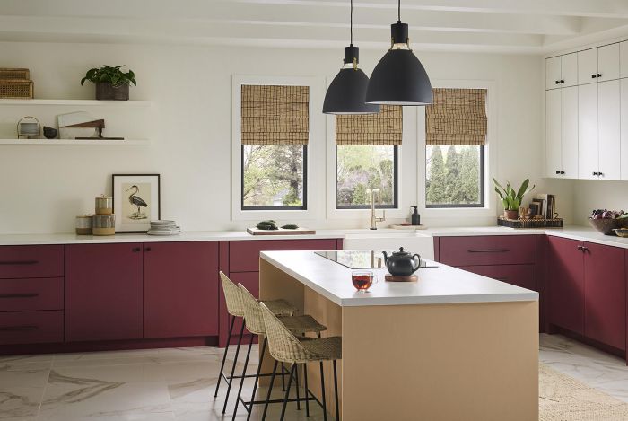 Cette image montre une cuisine qui s’affirme par la couleur rouge foncé des armoires du bas et l’îlot de couleur blond chamois, les matériaux naturels et les luminaires modernes noirs.