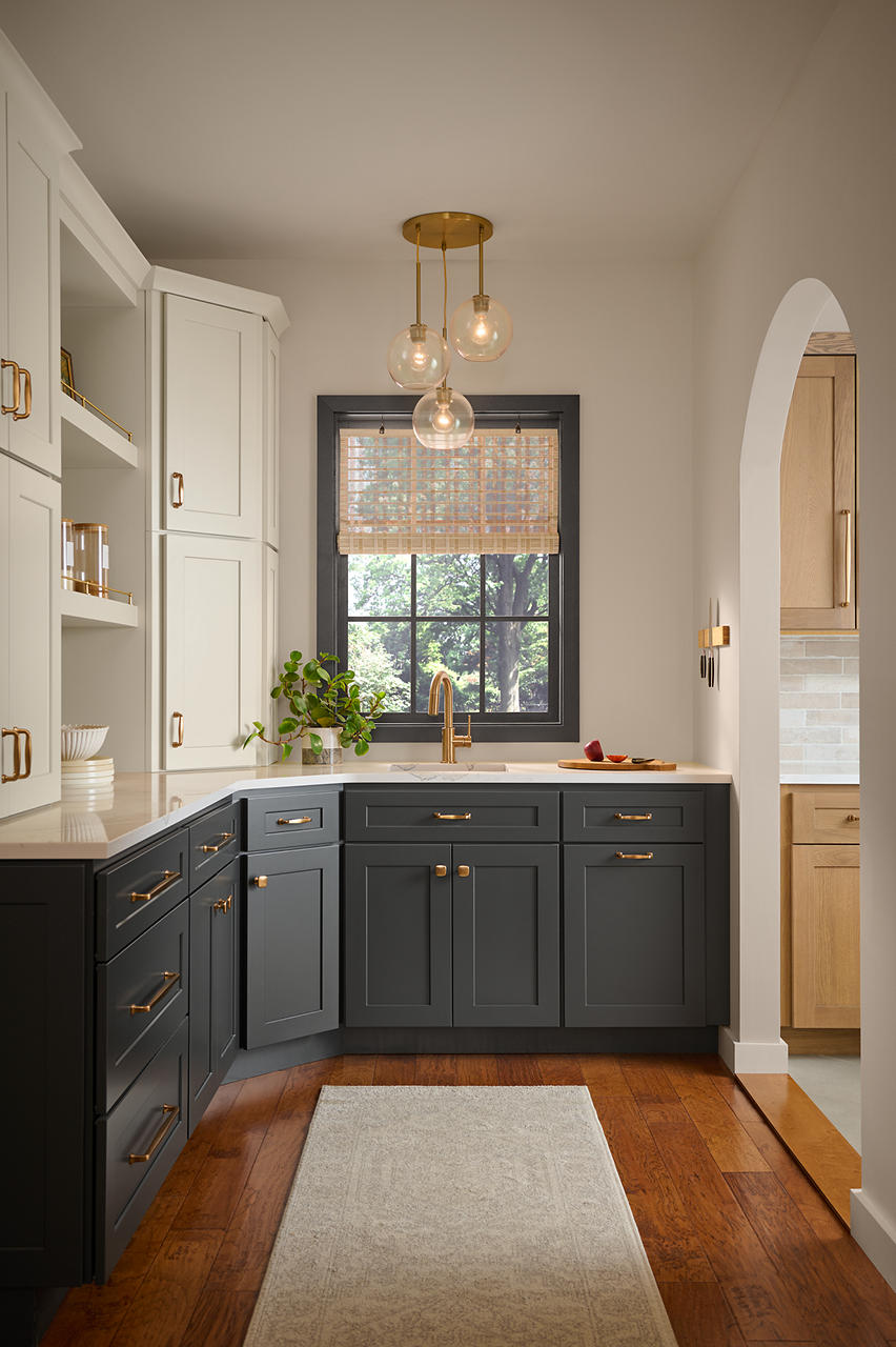 Cette image montre une pièce garde-manger avec des murs peints en Pain de blé, des armoires du bas de couleur foncée, une étagère encastrée de couleur blanche, des poignées en laiton, un parquet au ton chaud et une embrasure voûtée donnant sur la cuisine.