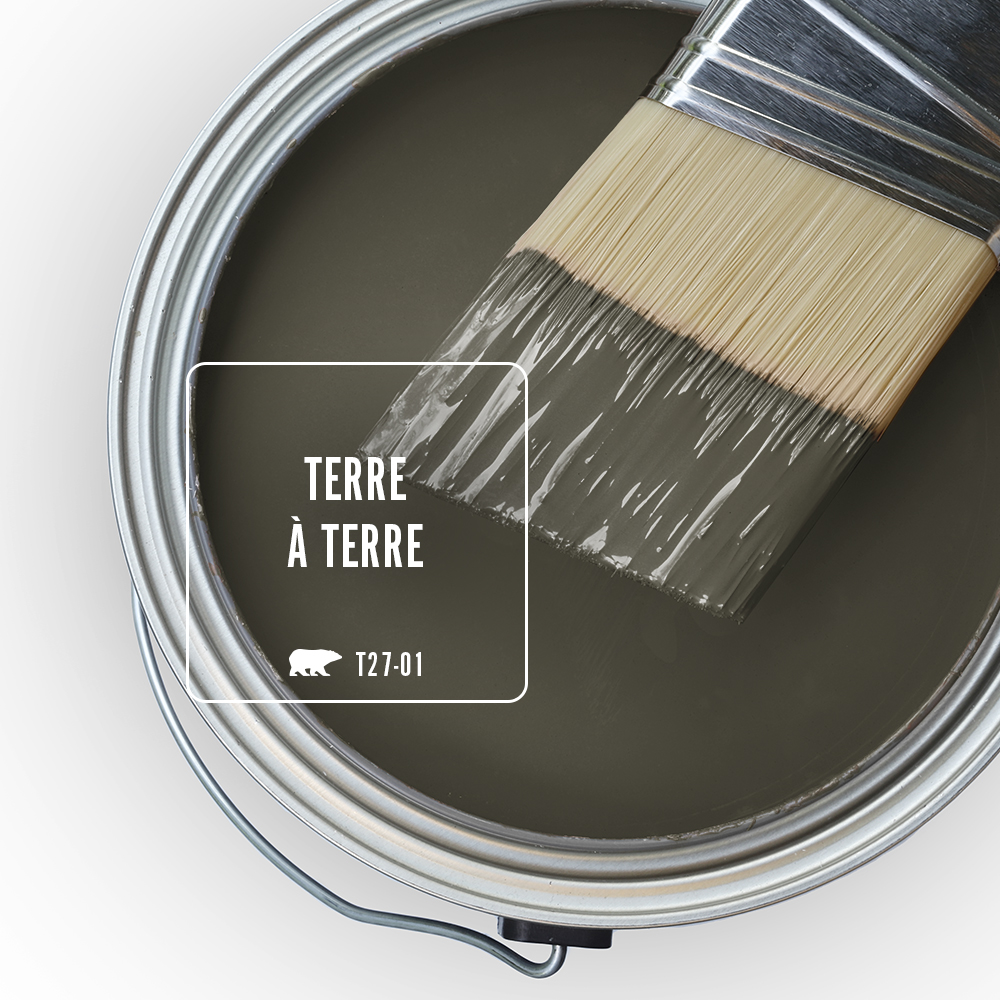 Cette image montre le dessus d’un pot de peinture ouvert rempli d’une peinture en teinte Terre à terre (T27-01) de BEHR. Un pinceau à moitié trempé dans la même couleur est posé sur le bord du pot.