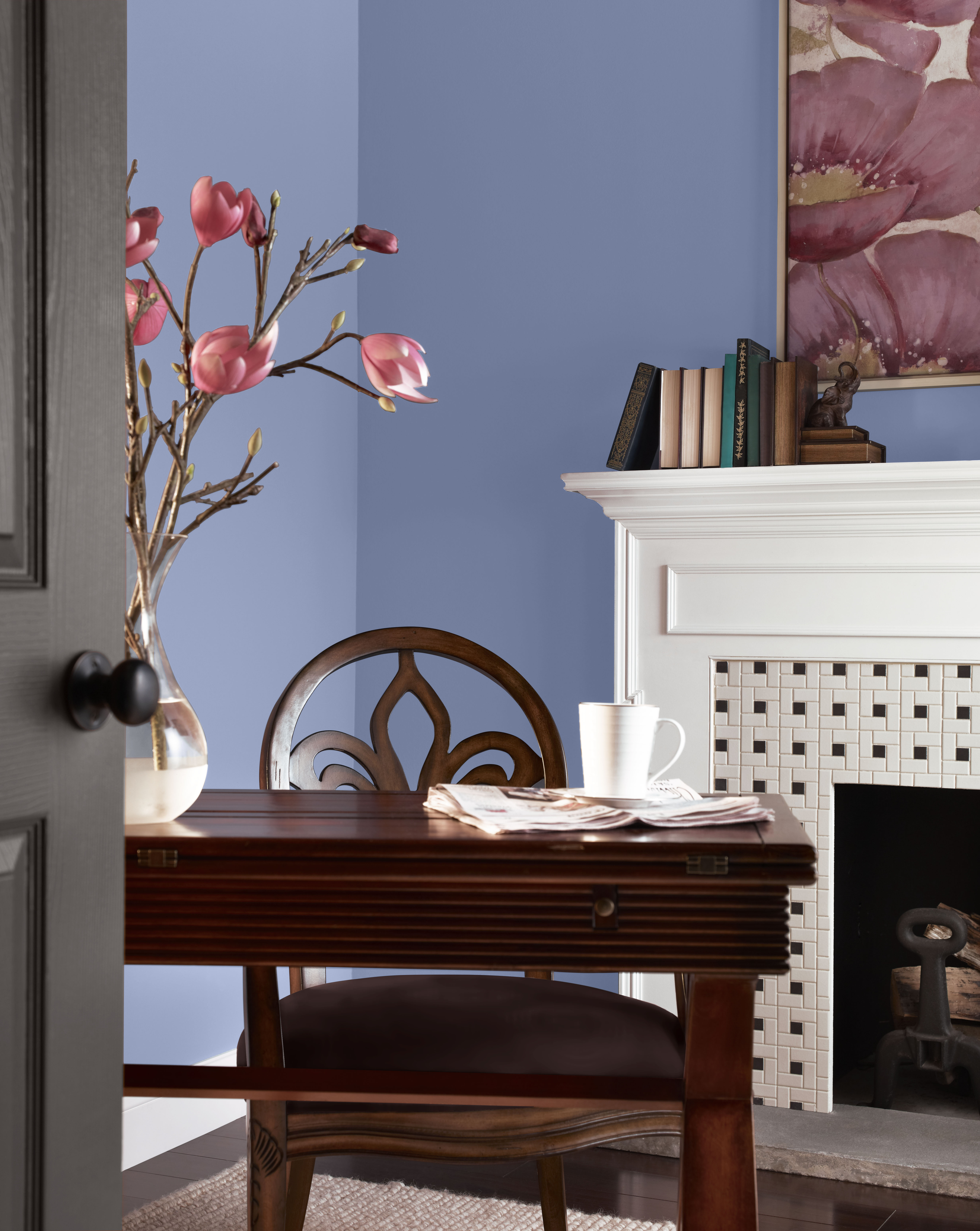 Cette image montre un espace de travail avec des murs peints en Ruban vintage, une nuance de bleu-violet poudré, ainsi qu’une cheminée au manteau blanc, un bureau en bois de couleur foncée, des touches de rose tendre ici et là et des éléments décoratifs d’inspiration ancienne, le tout dans un décor romantique de style Régence.