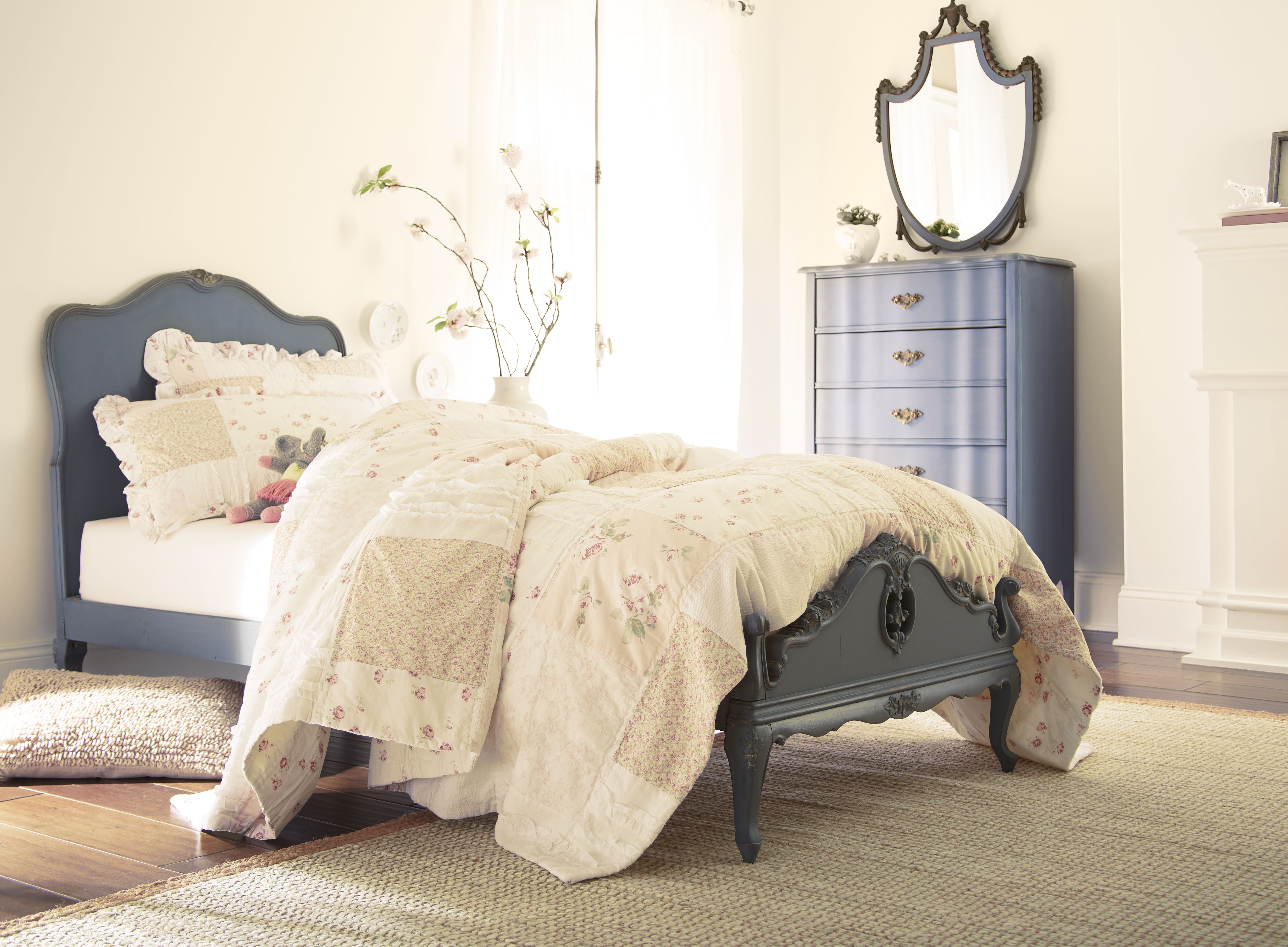 Cette image montre une chambre à coucher avec des murs crème peints en teinte Perle polie, un mobilier bleu de style ancien, incluant un lit recouvert d’une épaisse literie aux tons pâles, le tout inondé de lumière du jour et digne du plus pur romantisme.