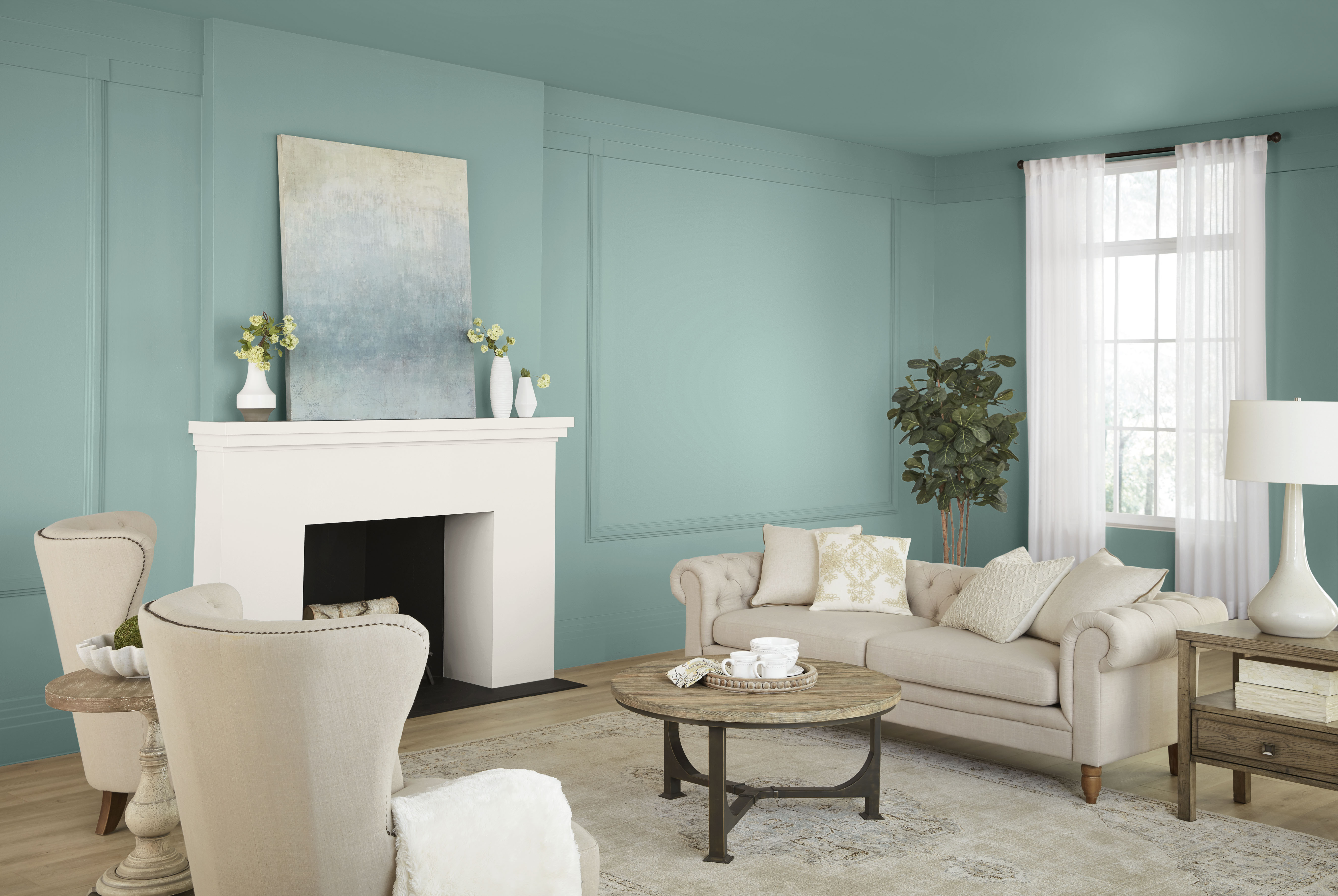 Cette image montre un salon dont les murs et le plafond sont peints en Soie opale, un élégant bleu-vert pâle, avec un manteau de cheminée blanc, des meubles rembourrés de couleur neutre, des matériaux naturels et de chaleureux accents de bois, le tout créant une symphonie de couleurs romantiques pour cet espace intérieur.