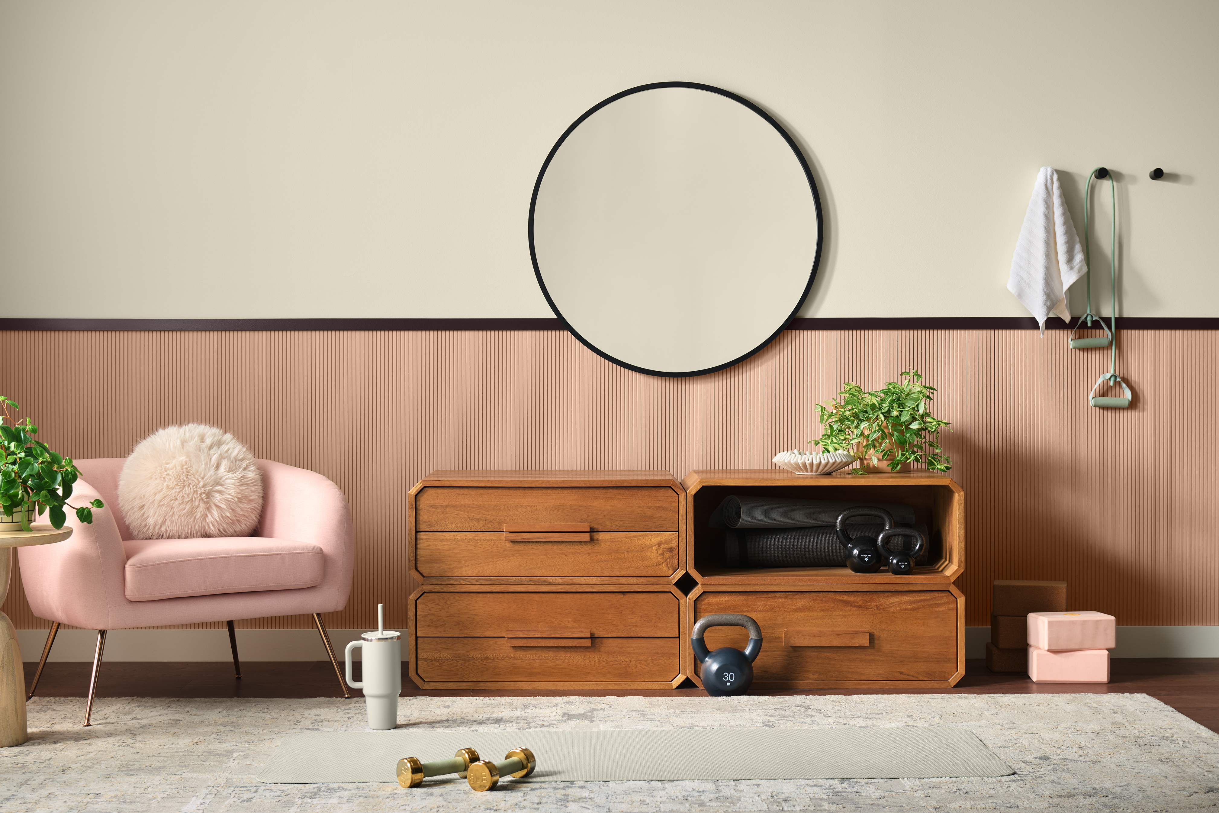 Cette image montre une pièce de yoga avec le mur du haut peint en Beige côtier (PPU7-13) et le mur du bas peint en Rose Sedona (S190-3). La pièce comprend un meuble de rangement en bois naturel, une chaise rose et des plantes d’intérieur, le tout dans un décor aux tons doux et neutres.