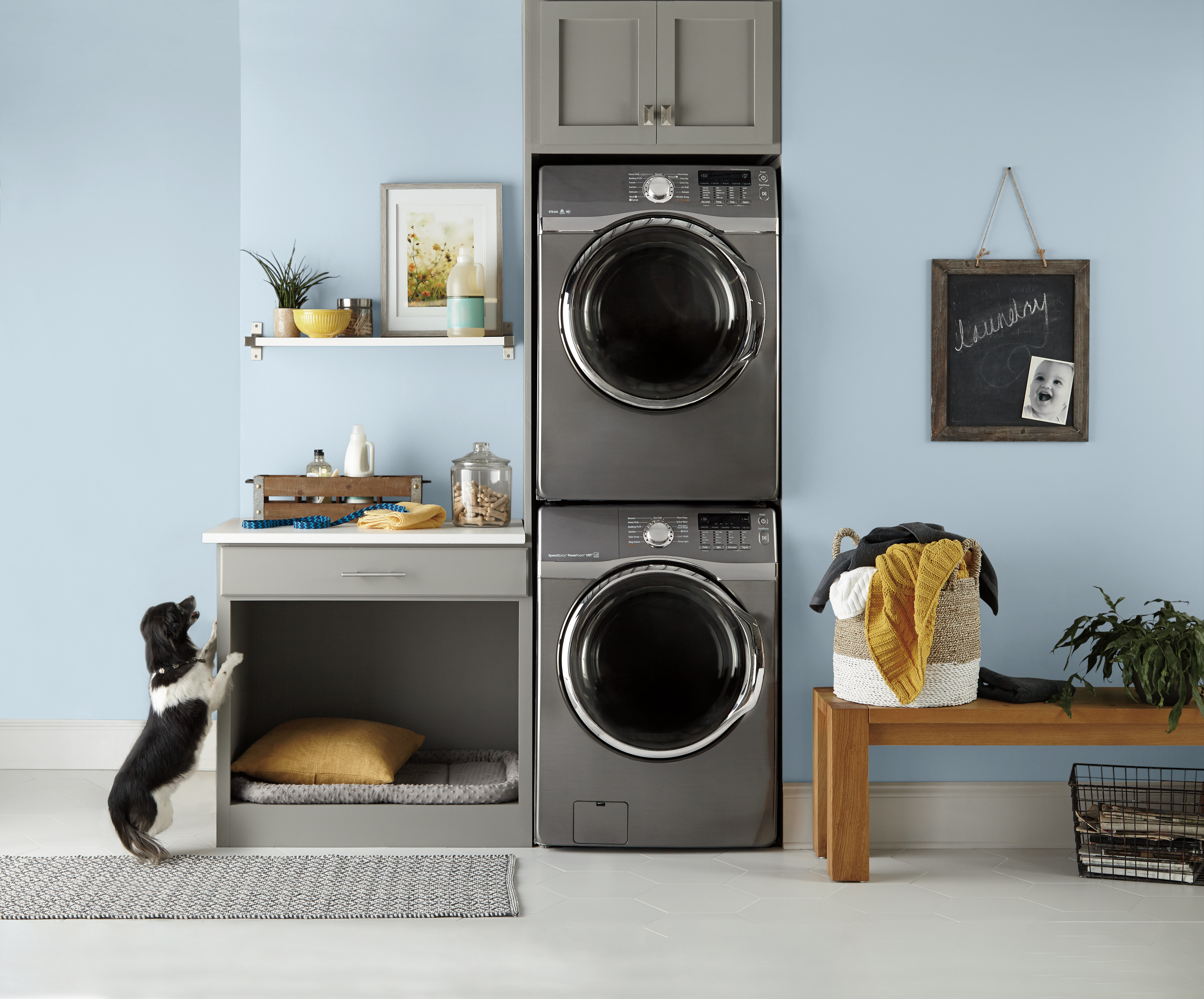 Cette image montre une salle de lavage dont les murs sont peints en Denim pâle (PPU14-15), un bleu clair inspiré de la couleur du ciel. On y voit également des armoires foncées, une tablette et un comptoir blancs, une table basse en bois aux tons chaleureux et des objets décoratifs en tissu.