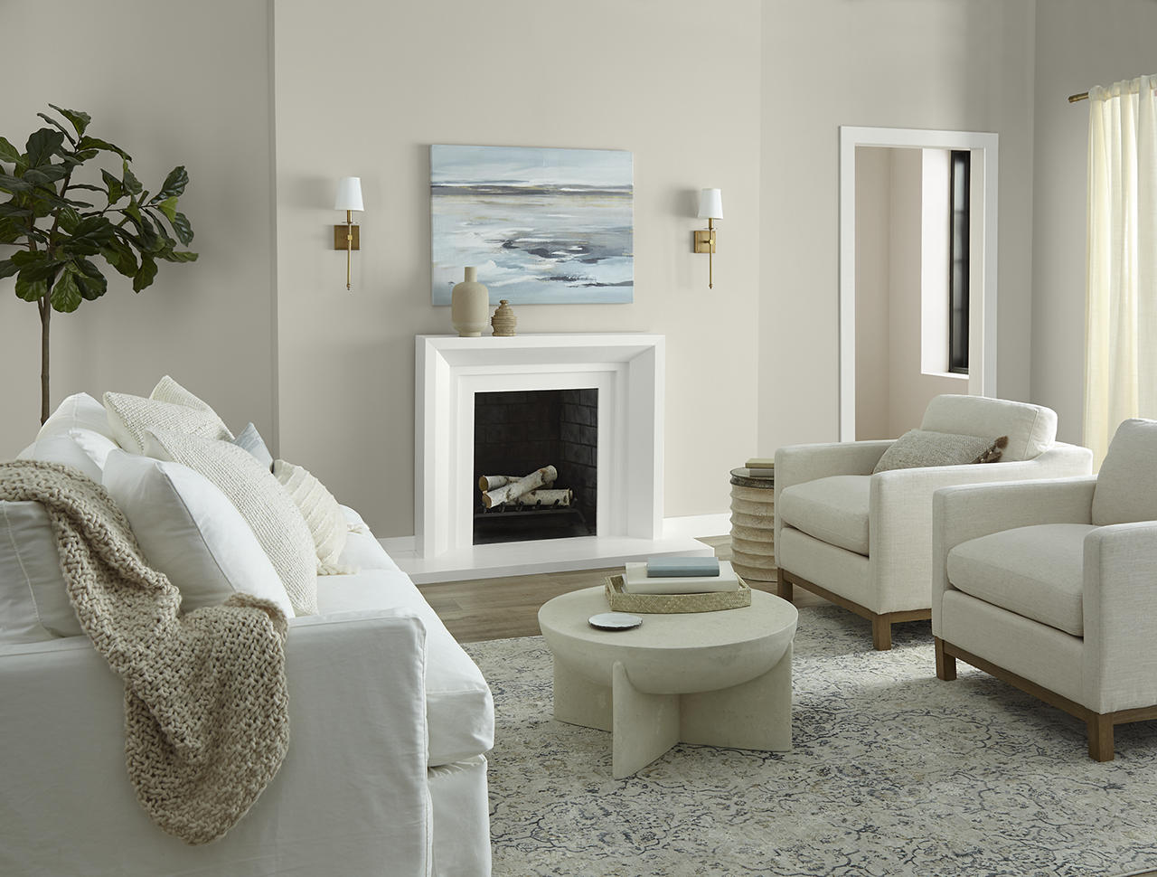 Cette image montre un salon lumineux et décontracté à l’allure subtilement côtière, où les murs sont peints en teinte Gris tranquille, un gris doux et chaleureux, tandis que le mur du couloir est peint en teinte Encore plus beige, et les garnitures, en teinte Crème fouettée. Les poutres apparentes au plafond, des meubles rembourrés blancs, un manteau de cheminée de style classique, des objets aux textures naturelles et une douce lumière du jour contribuent à créer un décor aéré et tout confort.