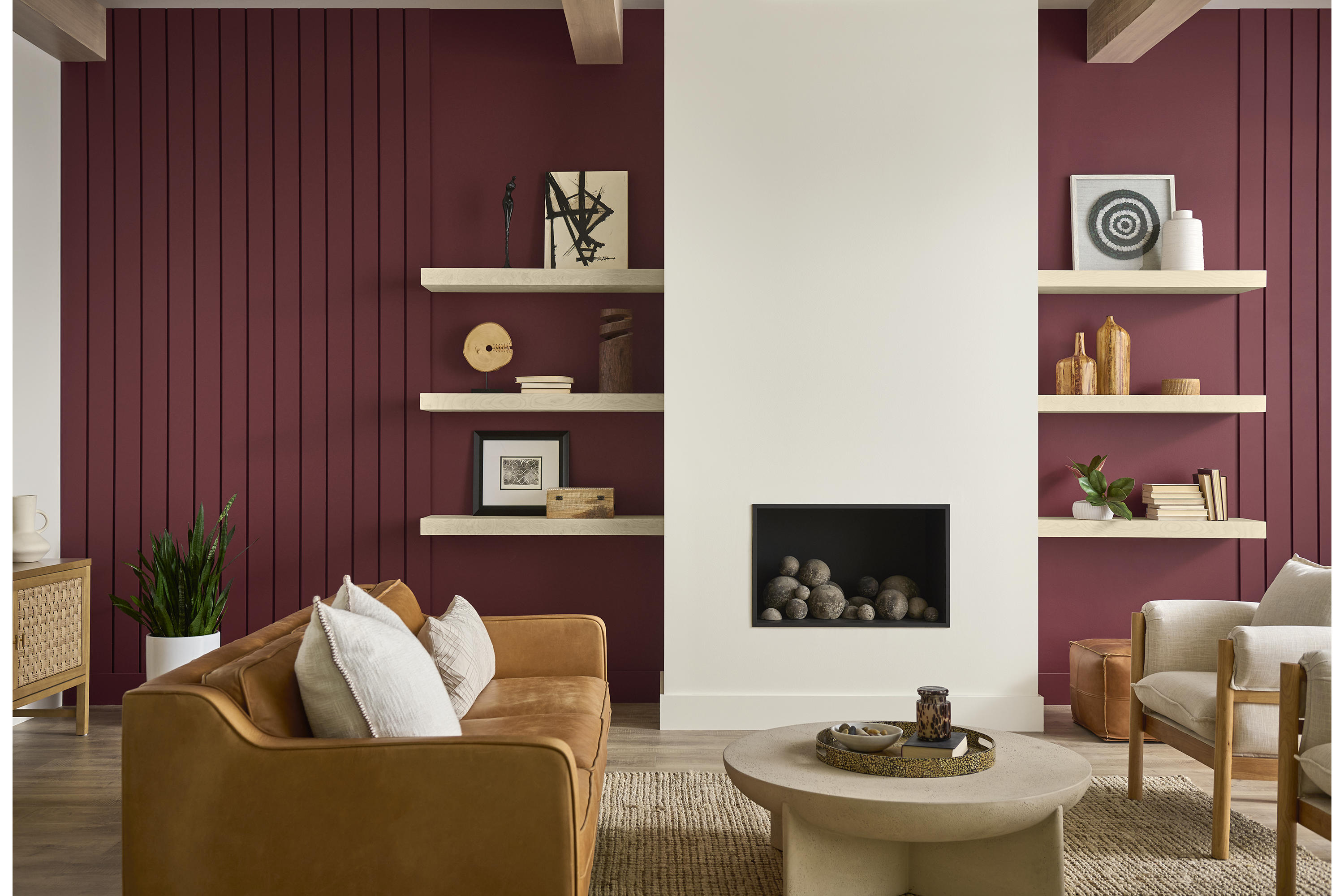 Cette image montre un salon dont le mur à cannelures verticales est peint en teinte Rumeurs de BEHRMD, un riche rouge rubis, avec un foyer peint en teinte Toile vierge, des meubles en bois au ton chaud ainsi qu’un divan et des fauteuils rembourrés aux couleurs neutres.