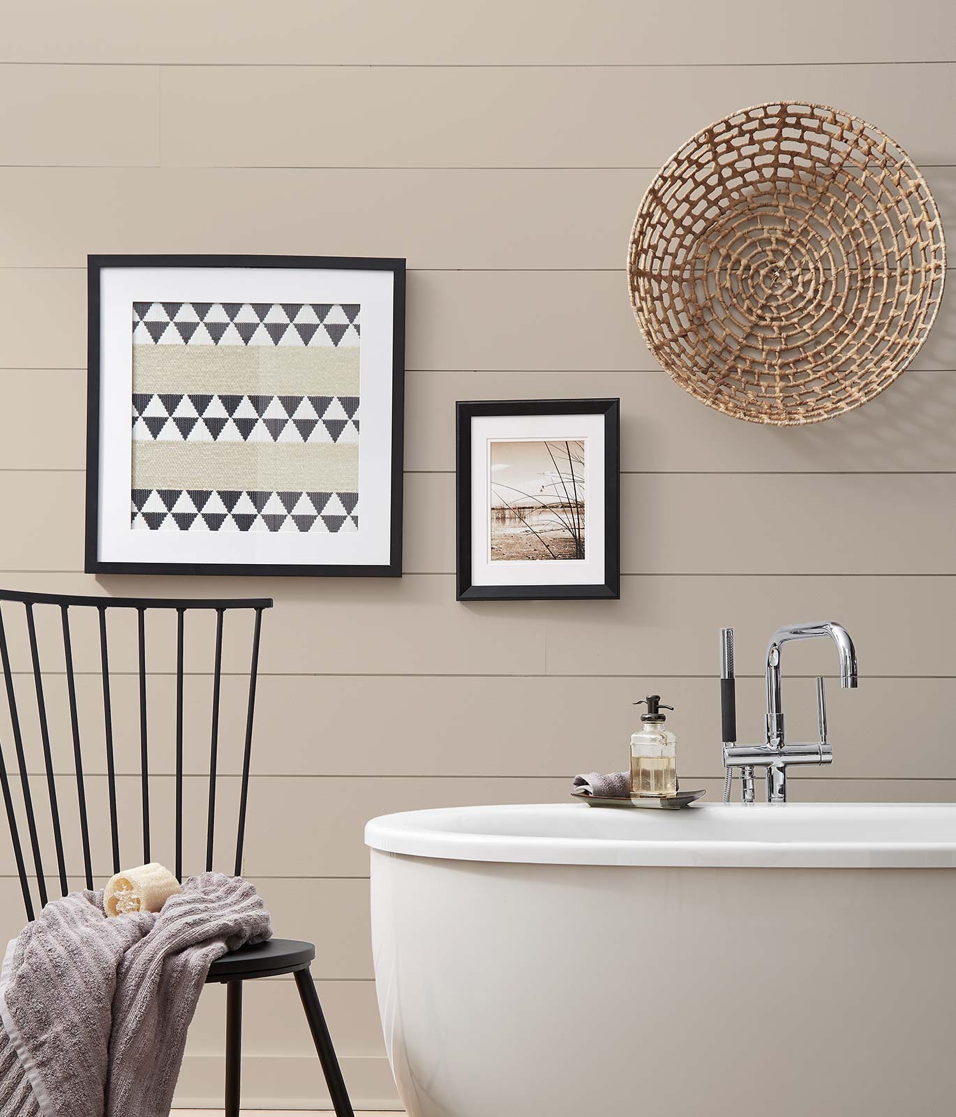 A bathroom painted in a beige color showing corner of a tub with a simple chair and blanket. Décor gives off a casual and comfortable feeling.