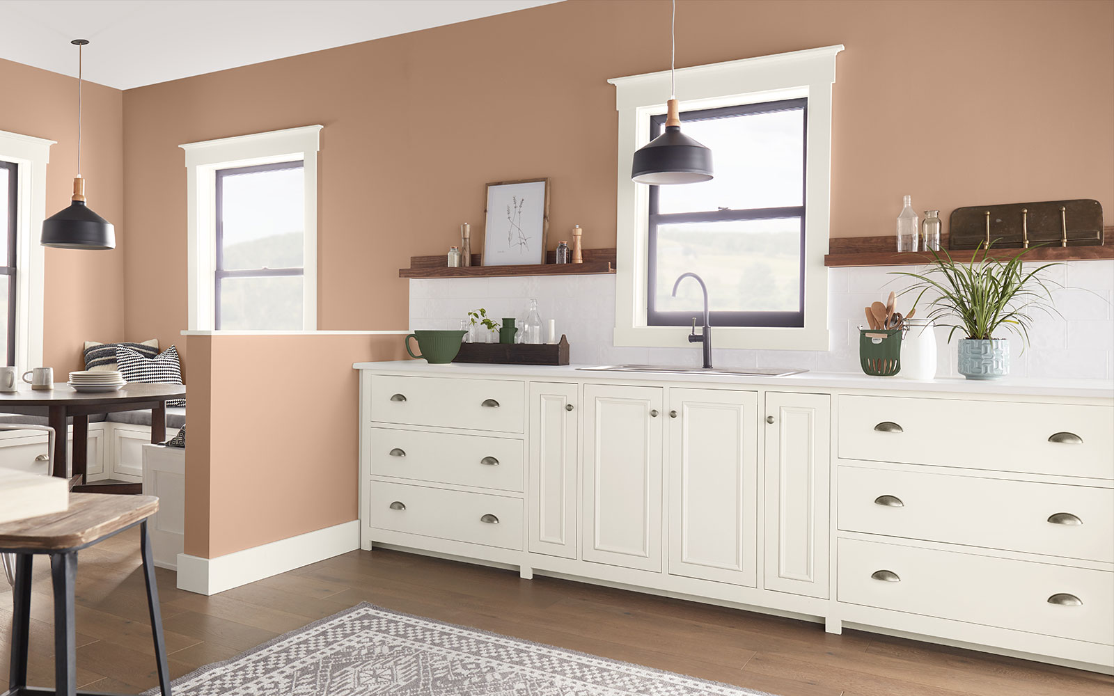 A kitchen image with three color swatches sitting beside it. The image displays the three colors: a dusty orange hue is used for the wall, a creamy white hue is used for the cabinets, and a dark green hue represents the plants sitting on the counters.