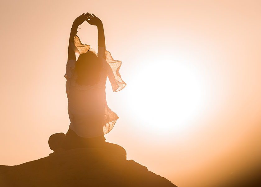 A woman sitting on the top of a mountain, meditating as the sun is setting behind her. The mood is tranquil.